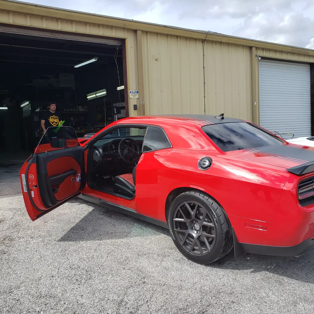 A Visions Glass Tinting technician in an XPEL shirt working on a red Dodge Challenger outside the open shop bay